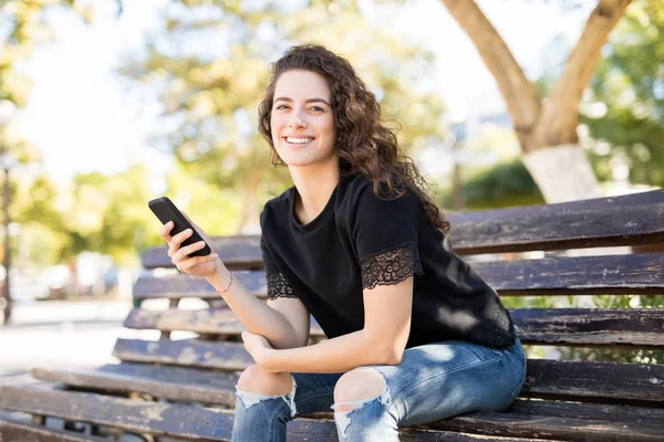 スマート フォンで公園のベンチに座っているスタイリッシュな若い女性 — ストック写真