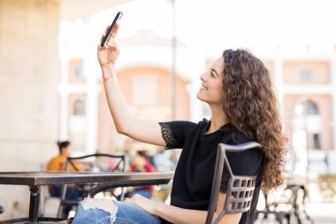 genç esmer bir selfie onun smartphone ile açık bir kafede otururken alarak