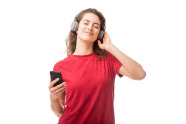 Beyaz arka plan üzerinde izole onun smartphone üzerinden müzik kulaklık giyen güzel genç kadın