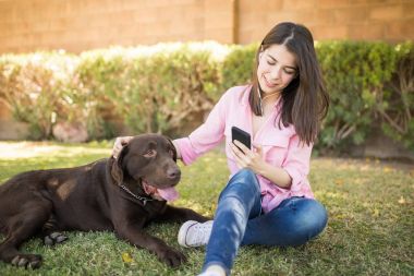 Kulaklık ve evcil köpek yanında smartphone ile parkta oturan kadın zevk