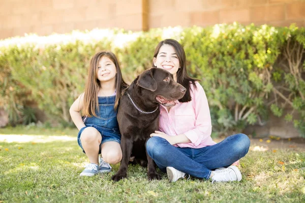 迷人的女人和可爱的小女孩坐在巧克力拉布拉多宠物狗坐在中心 — 图库照片