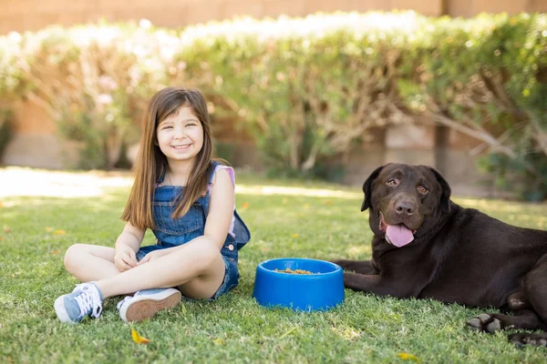 可爱的小女孩坐在公园里喂养她的狗在食物碗里 — 图库照片