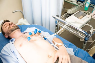 Genç adam göğsüne yerleştirilen EKG Elektrotları ile yatakta yatarken