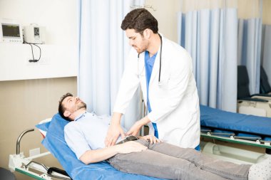 Yakışıklı genç doktor bir erkek hasta acile yatakta yatarken karın kontrol