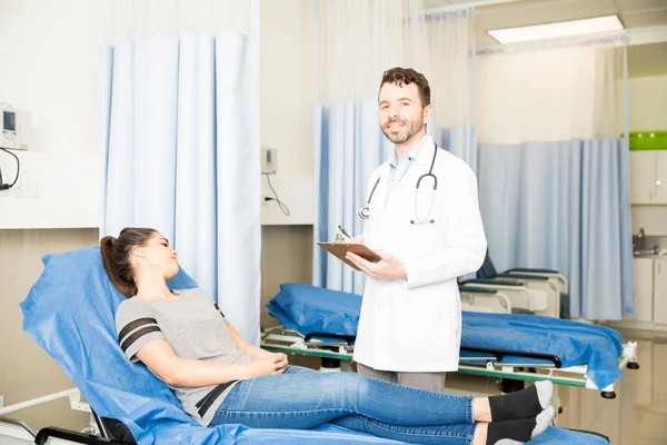 Portrait Handsome Latin Doctor Clipboard Standing Female Patient Lying Hospital — Stock Photo, Image