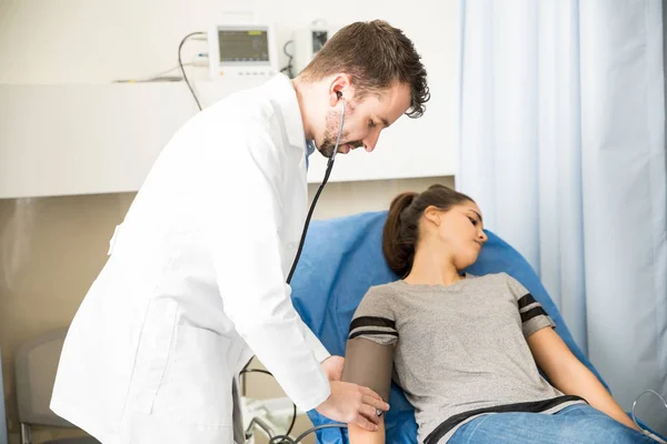 ハンサムな男性医師緊急治療室でベッドの上には 無意識のうちに横になっている女性患者の血圧測定 — ストック写真