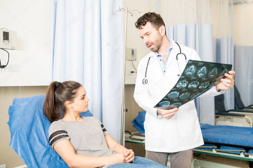 Radoilogist discussing at MRI scan results with female patient on bed in emergency room
