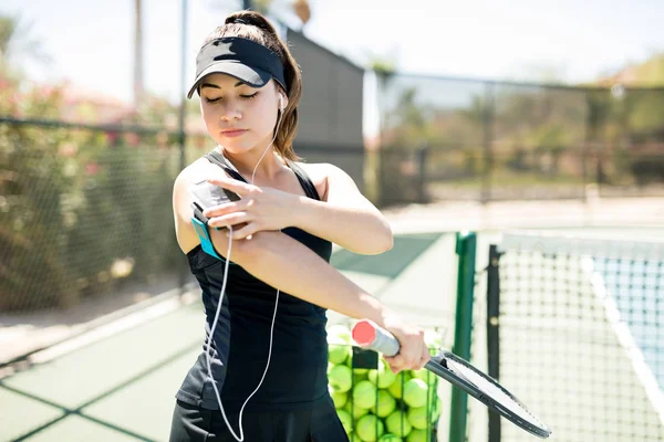 漂亮的年轻网球运动员选择正确的歌曲在她的智能手机开始她的网球场练习之前 — 图库照片