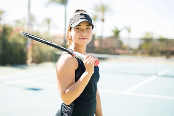 美丽的拉丁女子网球运动员的肖像站在球场上 她的肩膀上网球拍 并进行眼神接触 — 图库照片