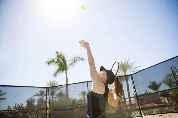 适合年轻女子网球运动员发球球 同时在球场上练习在一个晴朗的日子 — 图库照片