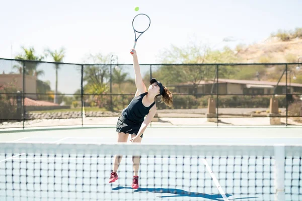 Good looking female tennis player training on the tennis court, hitting the ball overhead.