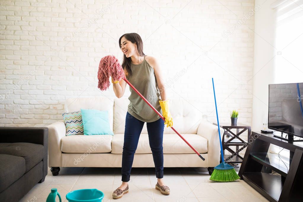 Young woman in protective gloves singing using mop and smiling while cleaning house