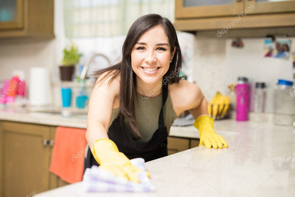 Smiling housekeeper cleaning table on kitchen background