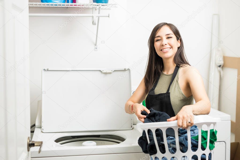 Young house maid wearing black apron putting clothes in machine for washing
