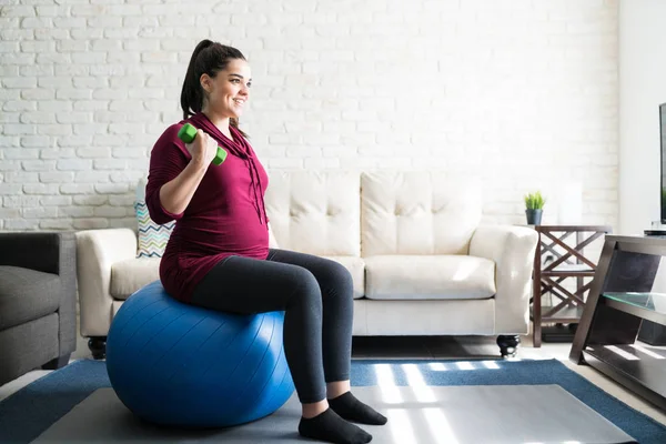 Full Length Smiling Beautiful Pregnant Woman Exercising Dumbbells While Sitting — Stock Photo, Image