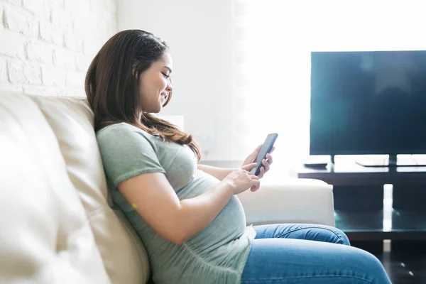 Mujer Bastante Embarazada Sonriendo Mientras Usa Teléfono Móvil Sala Estar — Foto de Stock