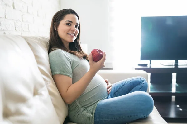 Mulher Grávida Lindo Segurando Maçã Fresca Enquanto Sentado Sofá Casa — Fotografia de Stock