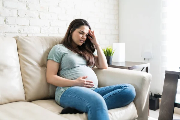可愛いです妊娠中の女性は頭痛とともにリラックスしながらソファでリビングルーム — ストック写真