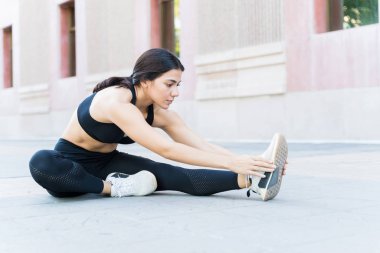 Çekici, genç, esnek bir kadın. Yaya yolunda egzersiz yaparken bacağını esnetiyor.
