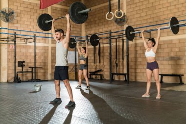 Spor salonunda spor yaparken halter kaldıran aktif genç atletik arkadaşlar.