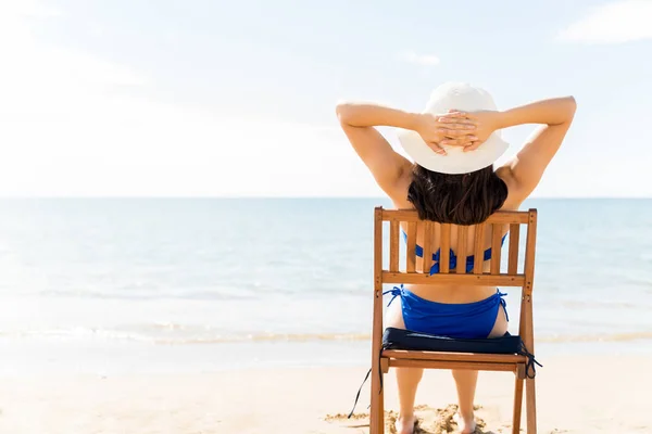 暑假期间 身穿比基尼 头戴礼帽坐在海滩椅子上的女性的背影 — 图库照片