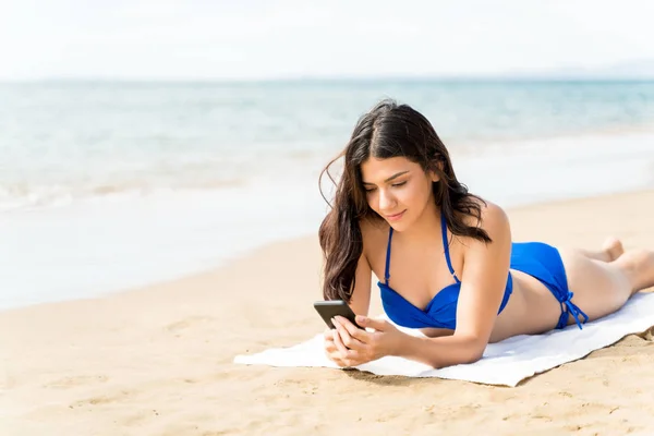 Donna Bikini Con Smartphone Sdraiata Sul Telo Mare Sulla Riva — Foto Stock