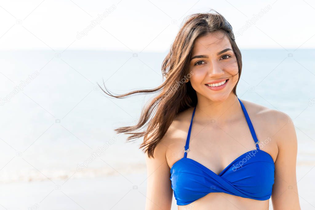 Attractive smiling woman wearing blue bikini enjoying wind at beach