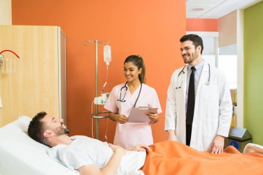 Gülümseyen Latin erkek ve kadın doktorlar hastanede hasta orta yaşlı bir hastayla konuşuyor.