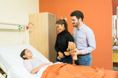 Gülümseyen aileler hastanede kızlarına oyuncak ayı veriyorlar.