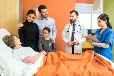 Male and female healthcare workers explaining disease to senior patient with family at hospital clipart