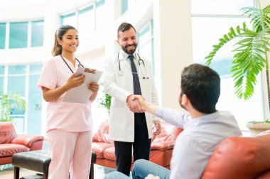Gülümseyen doktor, hastane lobisinde iyi haberler bekleyen bir adamla el sıkışıyor.