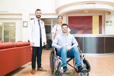 İyileşen orta yaşlı adam tekerlekli sandalyede otururken sağlık görevlileri hastanede lobide dikiliyorlar.