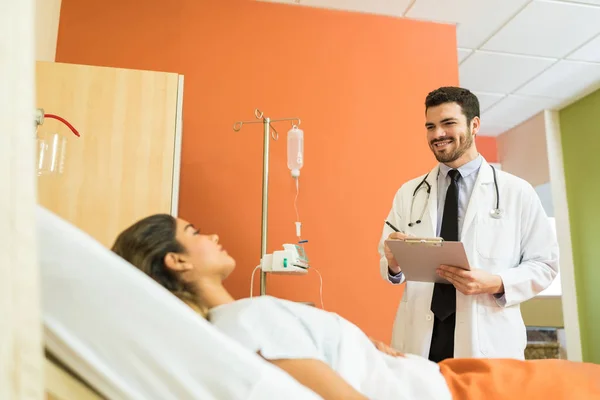 病院のベッドに横たわっ若い患者への医療報告を説明する中年の医師の笑顔 — ストック写真