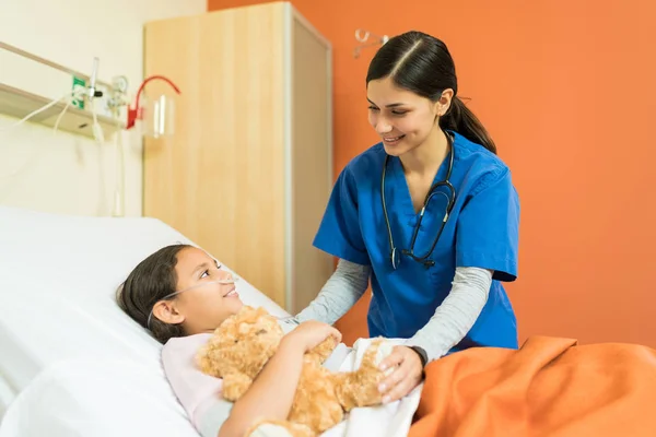 在治疗期间在医院病床上与小病人交谈的女护士 — 图库照片