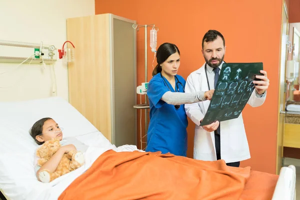 医护人员一边看X光 一边讨论病人躺在病床上的问题 — 图库照片