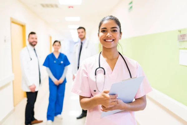 Bela Médica Sorridente Com Prancheta Contra Colegas Trabalho Fundo Hospital — Fotografia de Stock