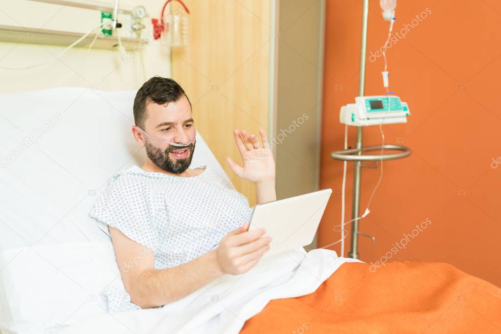 Smiling male patient waving while video conferencing on digital tablet at hospital