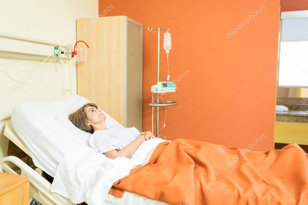 Thoughtful senior patient with IV drip lying on bed at hospital during treatment