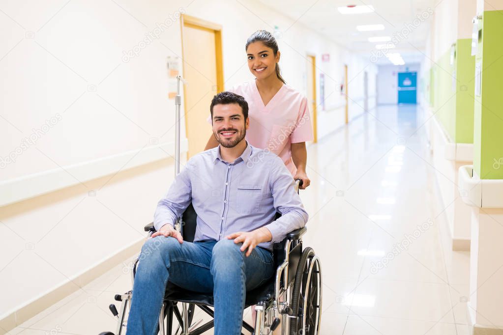 Smiling orderly pushing discharged mid adult patient on wheelchair at corridor in hospital