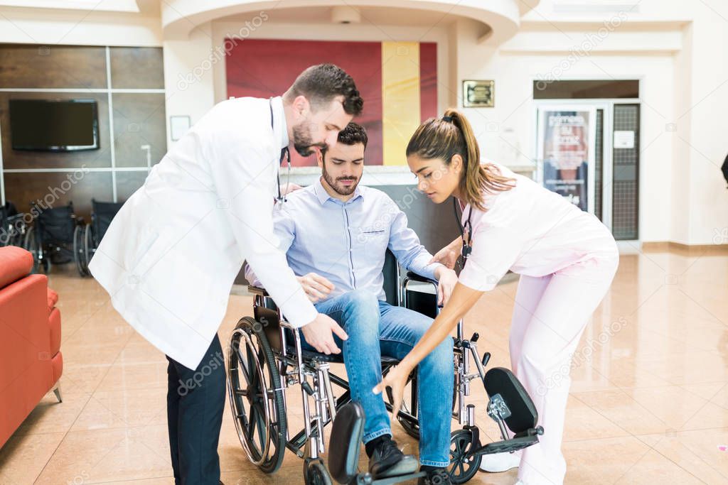 Male and female doctors helping patient to settle on wheelchair before leaving from hospital