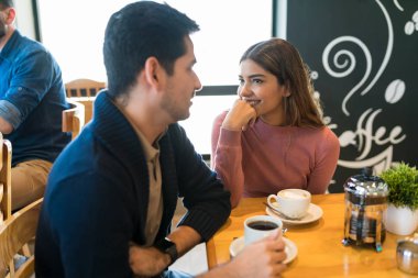 Restoranda kahve içerken erkek arkadaşına bakan gülümseyen bir kadın.