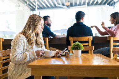 Kafkasyalı kadın, kafenin arka planında arkadaşlarıyla kahve içerken akıllı telefon kullanıyor.