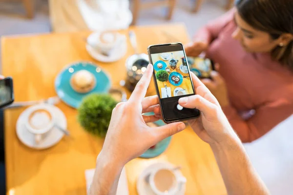 男人一边在智能手机上给甜点和咖啡拍照 一边和朋友们一起在咖啡店里享受 — 图库照片