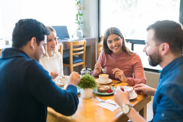 Male and female friends talking while enjoying coffee and dessert at table in cafe