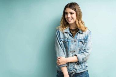 Kot ceketli, gülümseyen güzel bir kadın arka planda dikilirken gözlerini kaçırıyor.