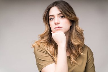 Kendine güvenen, eli çenesinde olan, arka planda göz teması kuran güzel bir kadın.