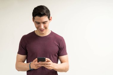 Gülümseyen çekici bir adam arka planda dururken cep telefonu kullanıyor.