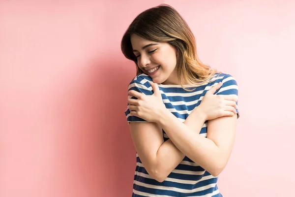 魅力的な幸せな若いです女性抱擁彼女自身として隔離されましたピンクの背景 — ストック写真