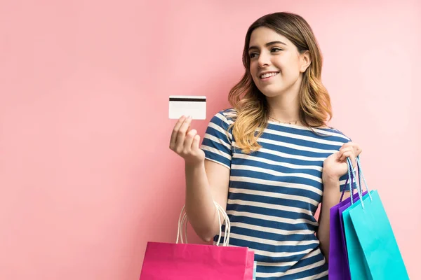 Young woman with credit card holding shopping bags against plain background