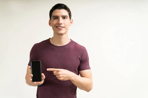 Knappe Jongeman Die Naar Smartphone Wijst Terwijl Hij Tegen Een — Stockfoto